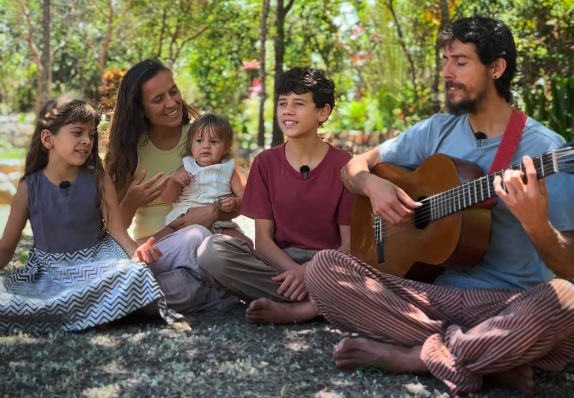 A família TerraTupy sentada ao ar livre, cantando e tocando violão